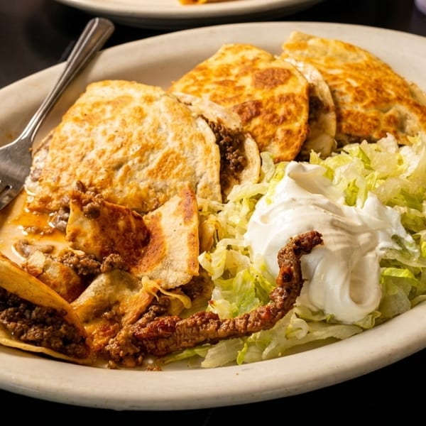 A plate of beef quesadillas and tacos with shredded lettuce and a dollop of sour cream.