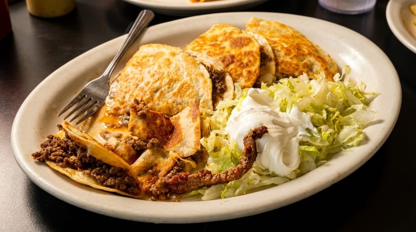 A plate of beef quesadillas and tacos with shredded lettuce and a dollop of sour cream.
