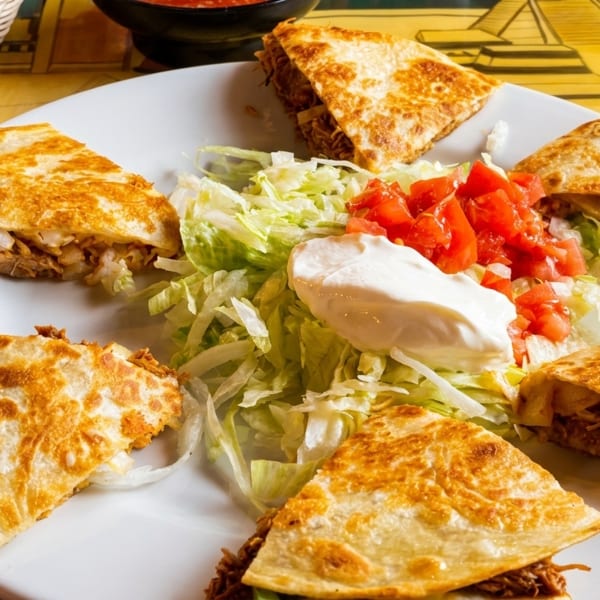 A white plate with six quesadilla wedges, shredded lettuce, diced tomatoes, and a dollop of sour cream.